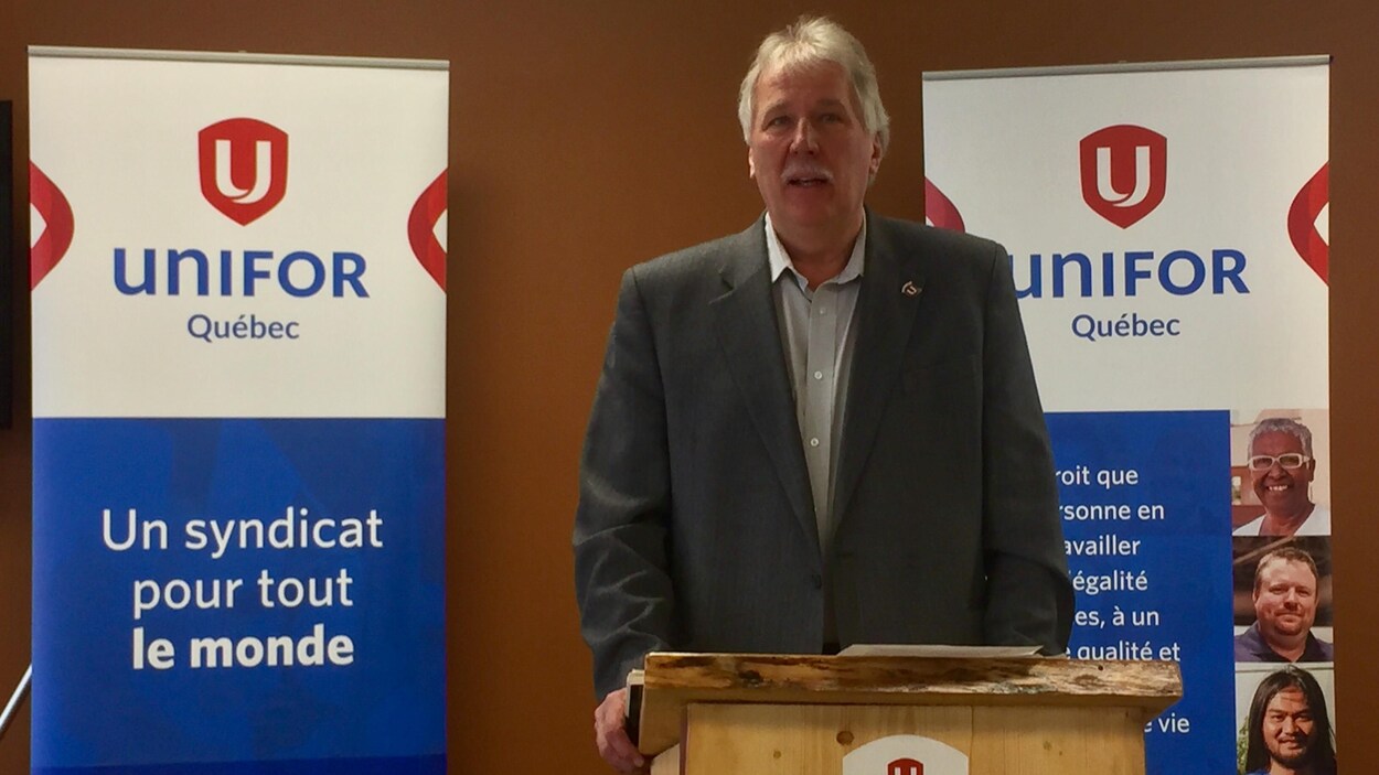 Un homme parle au lutrin, devant des affiches d'Unifor Québec. Un homme parle au lutrin, devant des affiches d'Unifor Québec.