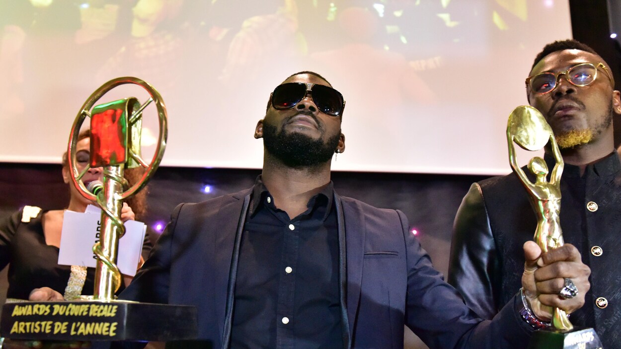 L'homme porte des lunettes noires et pose avec un trophée dans chaque main.