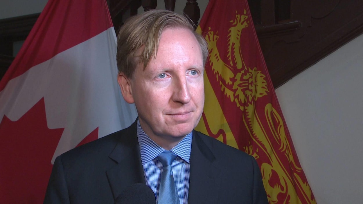 Dominic Cardy devant des drapeaux du Nouveau-Brunswick et du Canada.