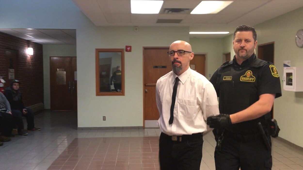 Donald MacHaight menotté avec un agent de police derrière lui.