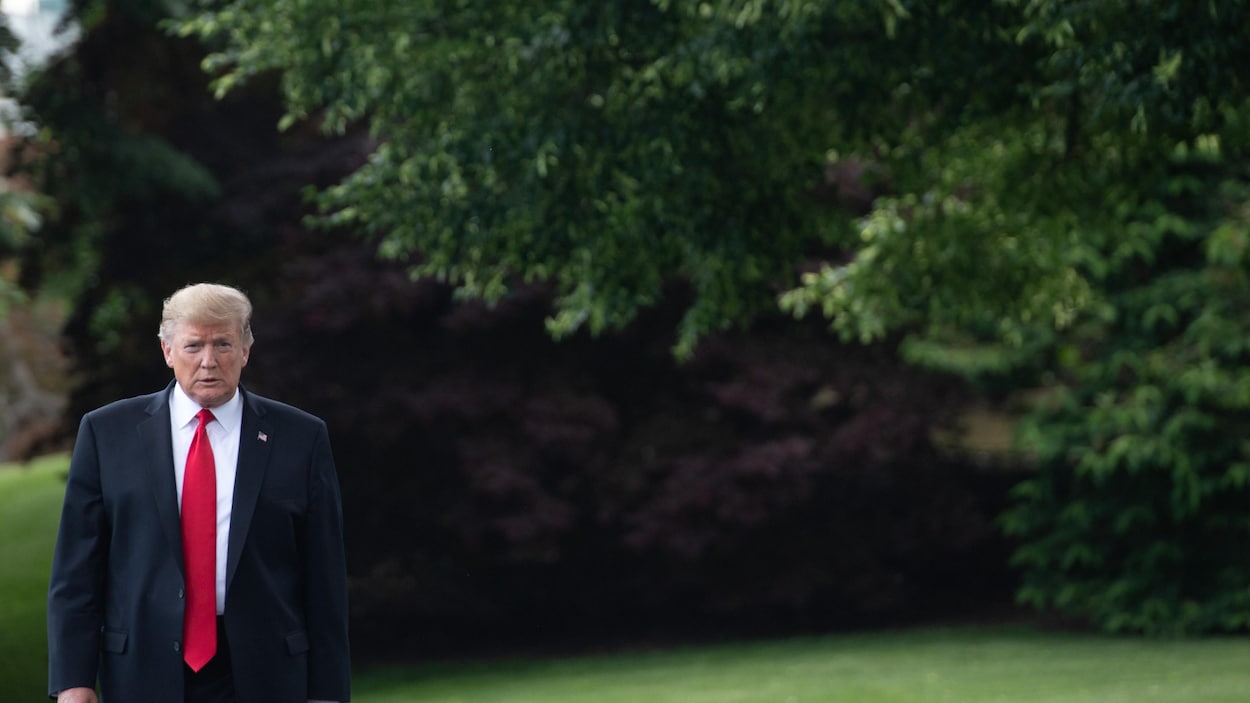 Donald Trump, portant un complet et une cravate, marche dans un jardin de la Maison-Blanche.