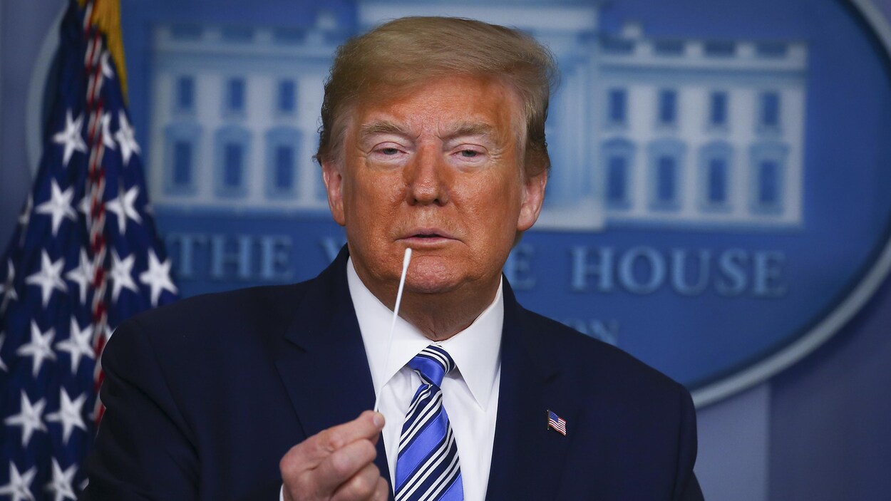Donald Trump, en conférence de presse, tient un écouvillon dans sa main.