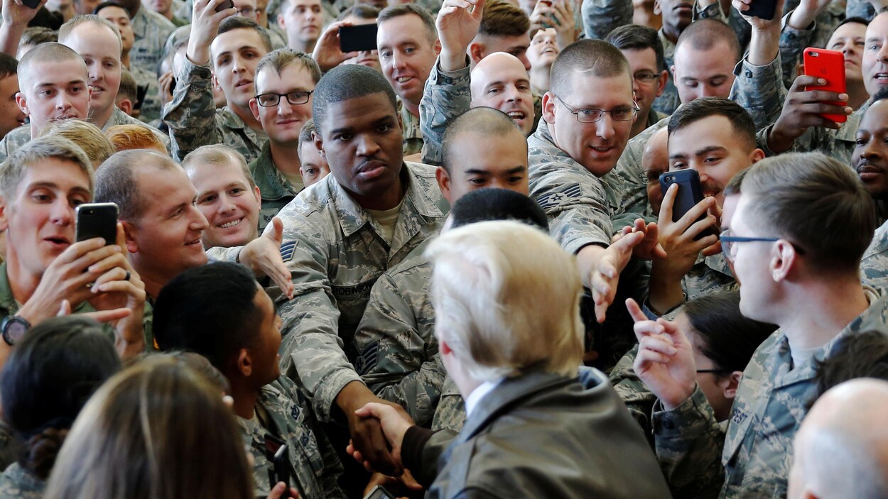 Donald Trump, qui est entouré de dizaines de militaires, serre la main de l'un d'entre eux, tandis que d'autres lui tendent la main. Donald Trump, qui est entouré de dizaines de militaires, serre la main de l'un d'entre eux, tandis que d'autres lui tendent la main.