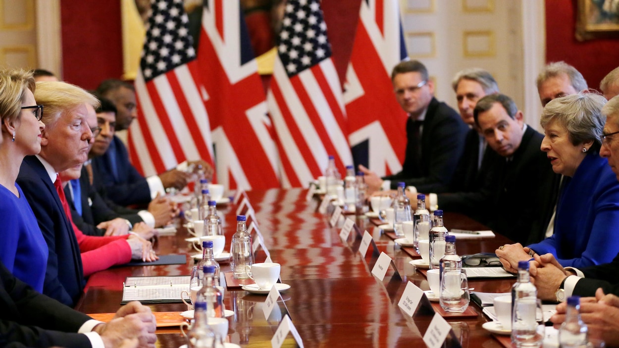 Donald Trump et Theresa May sont assis à une table de réunion avec plusieurs personnes.