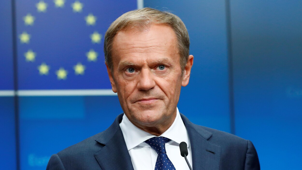 Donald Tusk montre un air sérieux derrière un micro.
