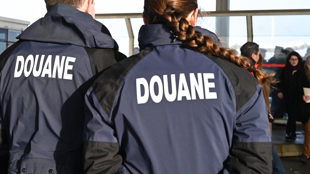 Des douaniers de dos observent des voyageurs.