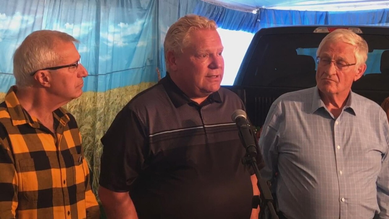Doug Ford est entouré de deux hommes.