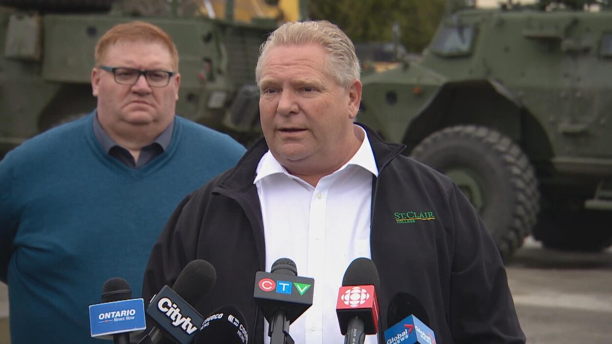 Doug Ford répond devant les micros des journalistes devant des chars de l'armée, aux cotés du maire de Bracebridge.
