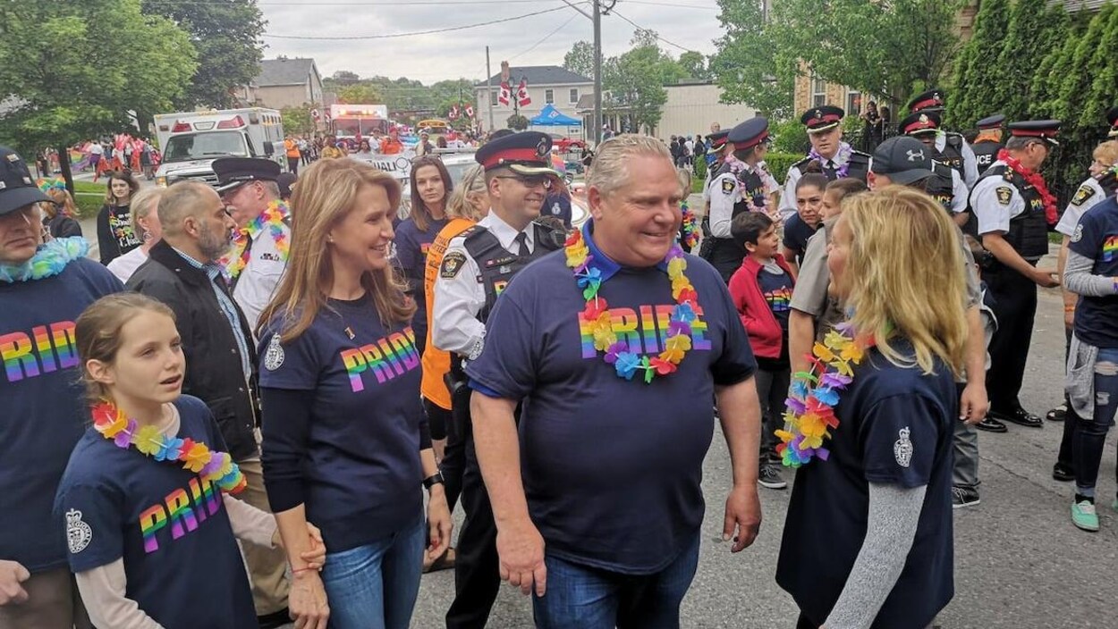 Doug Ford marche dans la foule dans la rue avec un tshirt aux couleurs LGBTQ+.