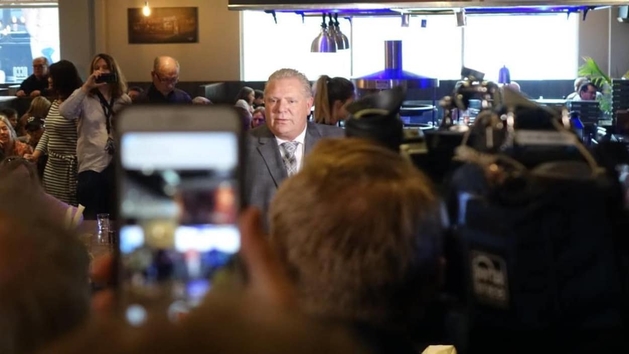 Doug Ford dans un restaurant entouré de plusieurs militants qui le photographient.