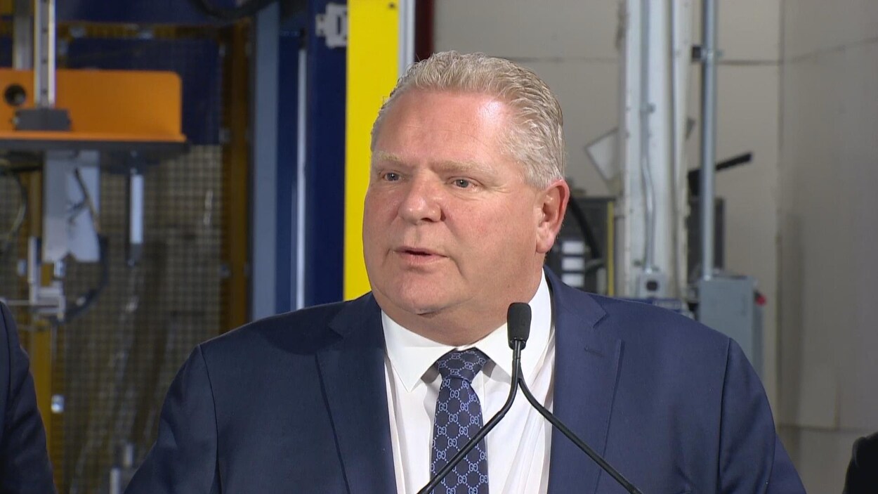 Photo d'un homme en complet bleu aux cheveux courts et blonds devant un micro