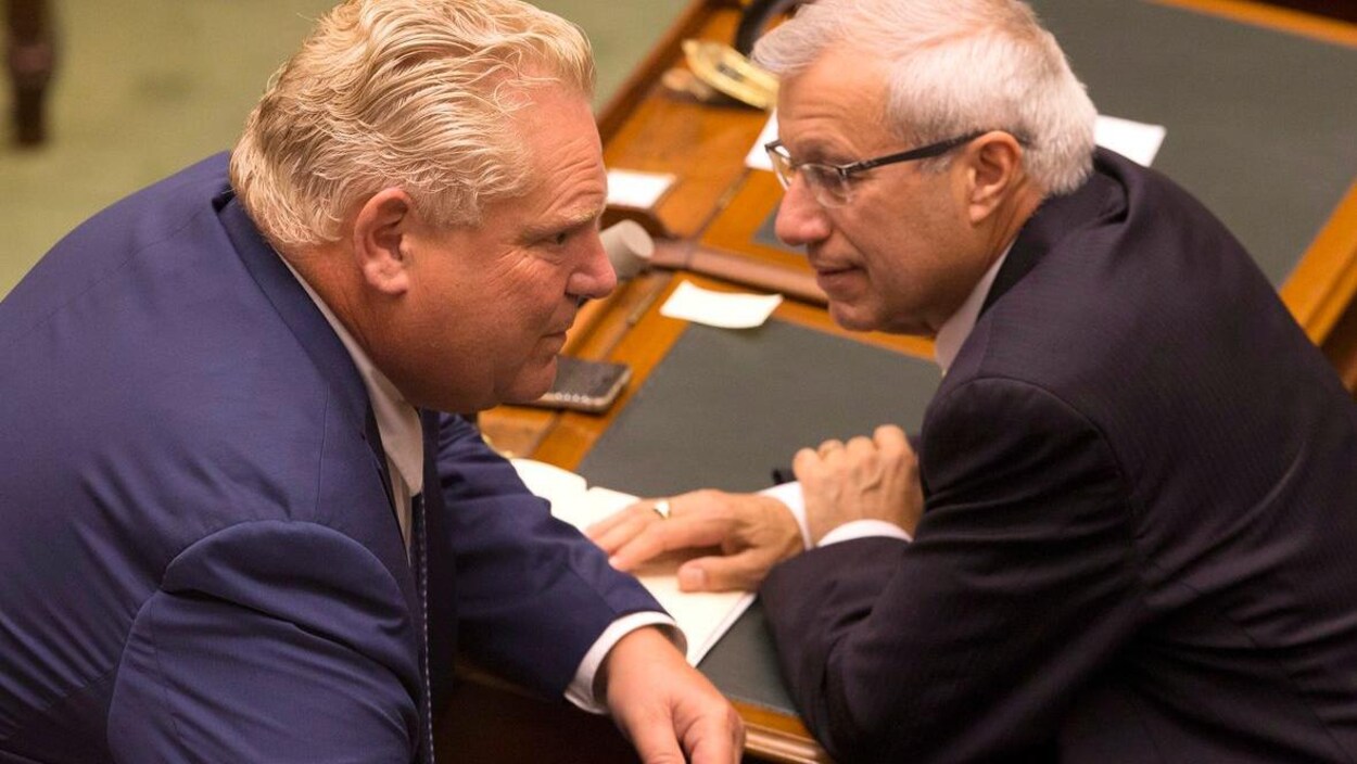 Photo de deux hommes en complet qui sont penchés l'un vers l'autre pour se parler dans l'oreille.