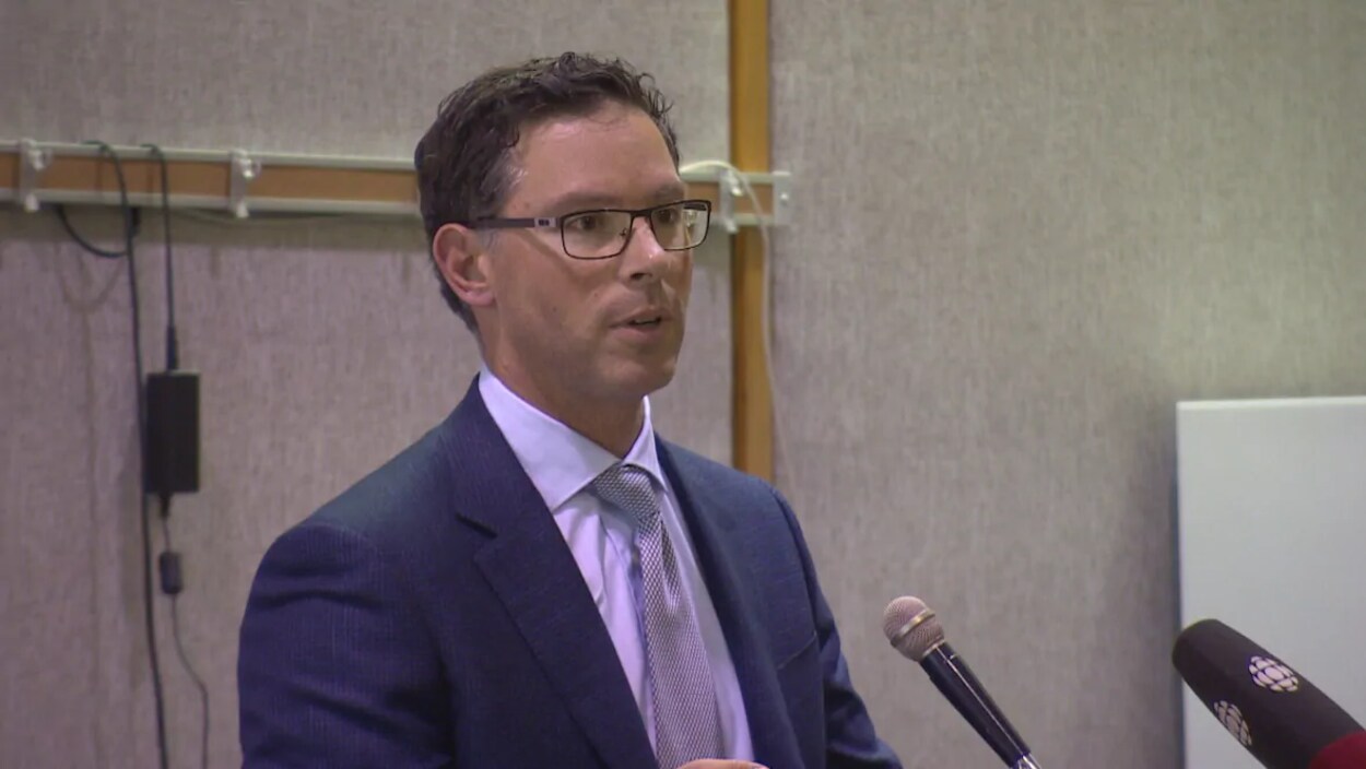 Le ministre Doug Schweitzer en complet debout devant un micro.