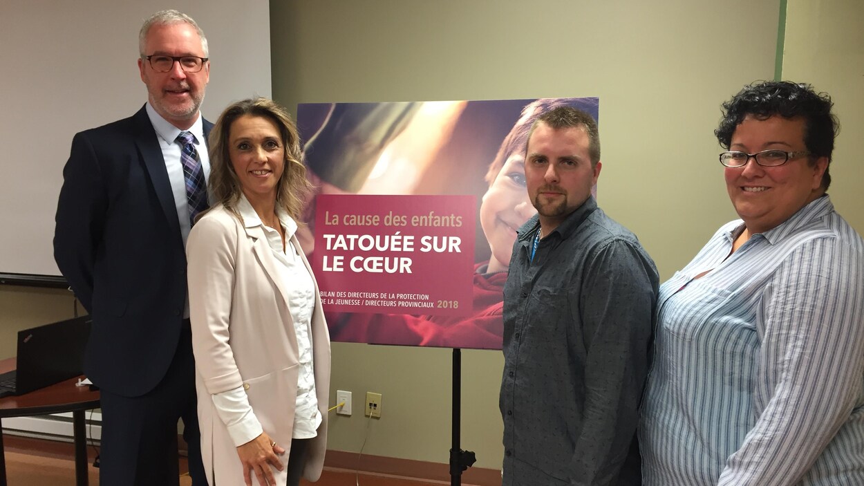 Deux hommes et deux femmes posent autour d'Une affiche disant «La cause des enfants tatouée sur le coeur». Deux hommes et deux femmes posent autour d'Une affiche disant «La cause des enfants tatouée sur le coeur».