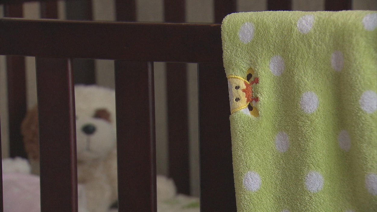 Un lit d'enfant avec une couverture verte. En arrière, se trouve une peluche.