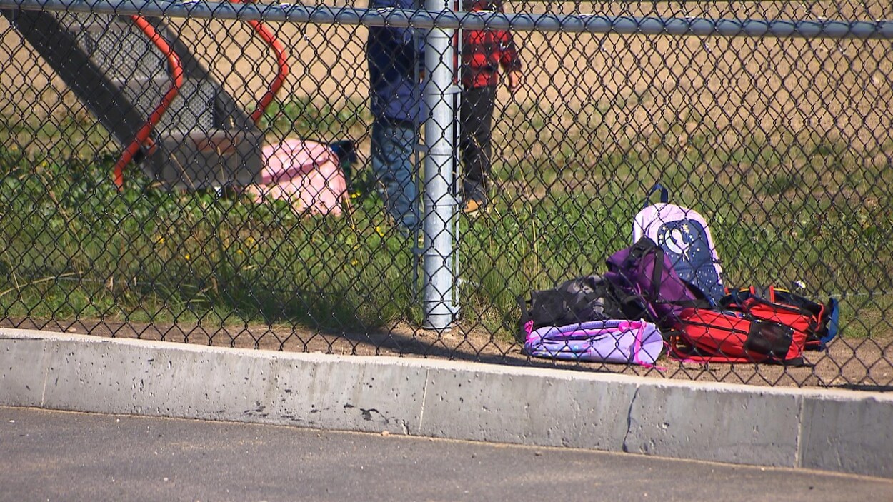 Des sacs à dos sont déposés sur le sol d'une cour d'école.