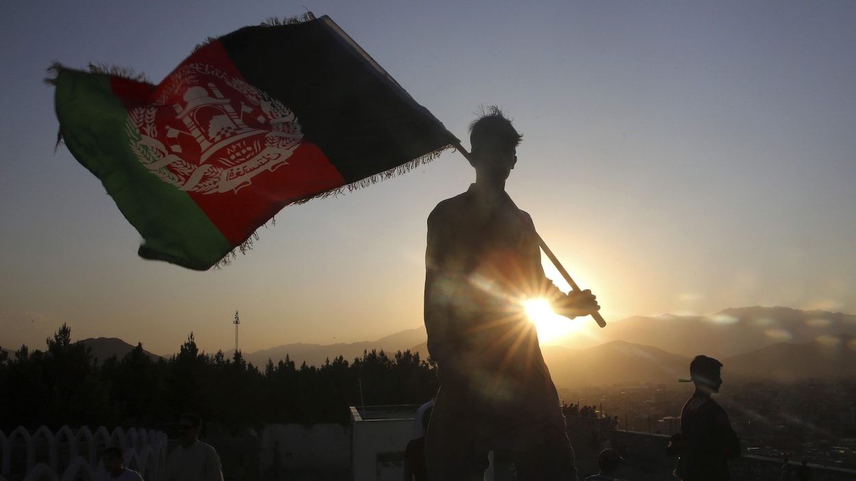 Un jeune homme porte un drapeau afghan sur son épaule.
