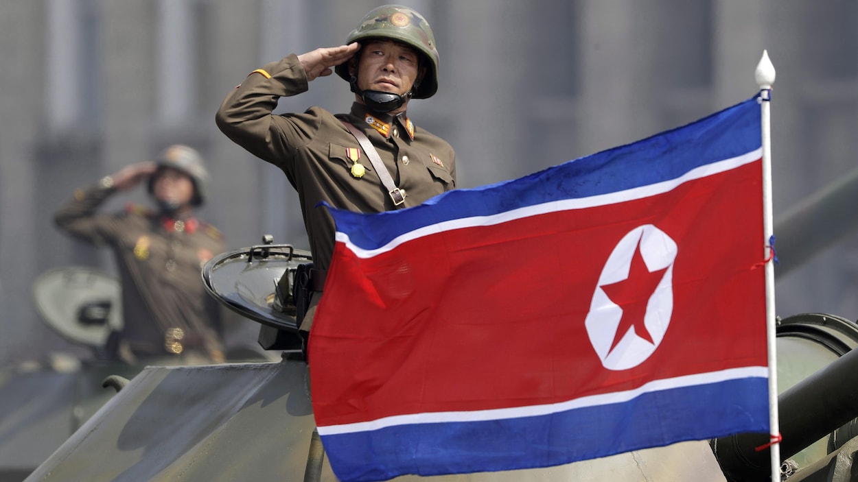 Un soldat faisant le salut militaire dans un char d'assaut. Devant lui, le drapeau nord-coréen.
