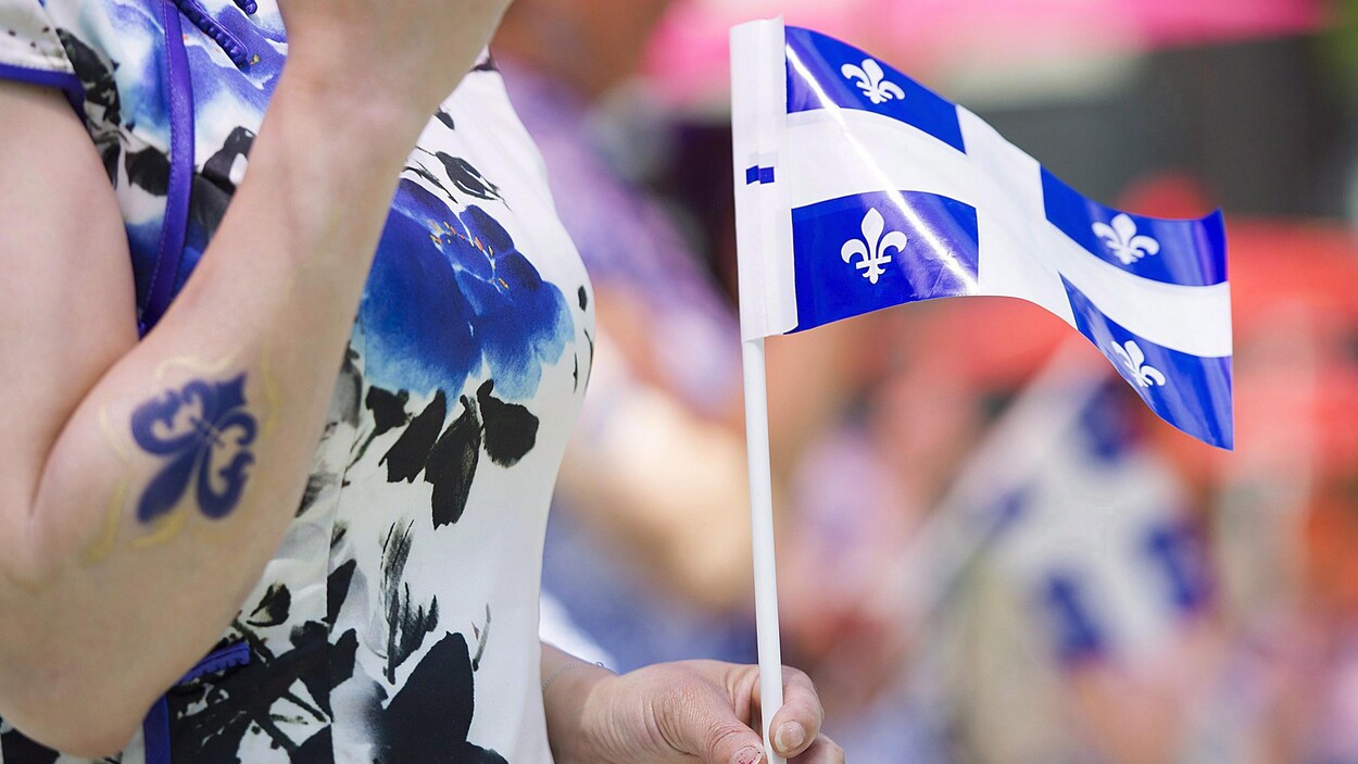 Une femme habillée de noir, blanc et bleu tient un drapeau du Québec.