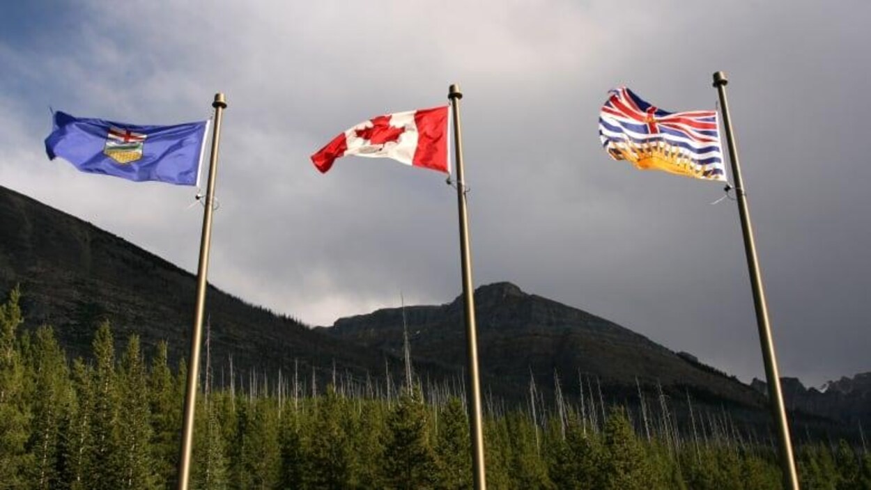 Trois drapeaux côte à côte dans le vent, un de l'Alberta, un du Canada et un de la Colombie-Britannique.