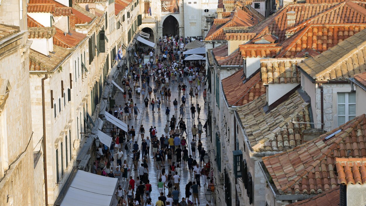 Vue en hauteur d'une rue piétonne de la vieille ville de Dubrovnik où des dizaines de touristes s'entassent. Vue en hauteur d'une rue piétonne de la vieille ville de Dubrovnik où des dizaines de touristes s'entassent.