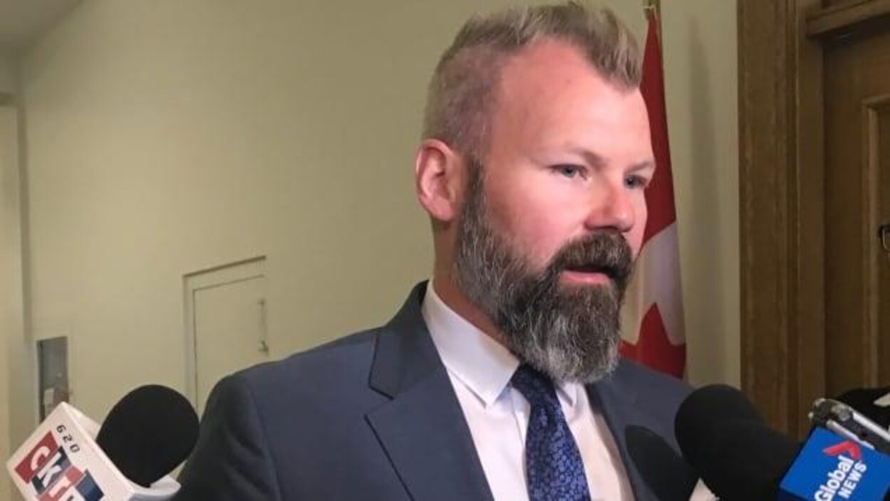 Un homme barbu donne une entrevue à des journalistes dans un couloir.
