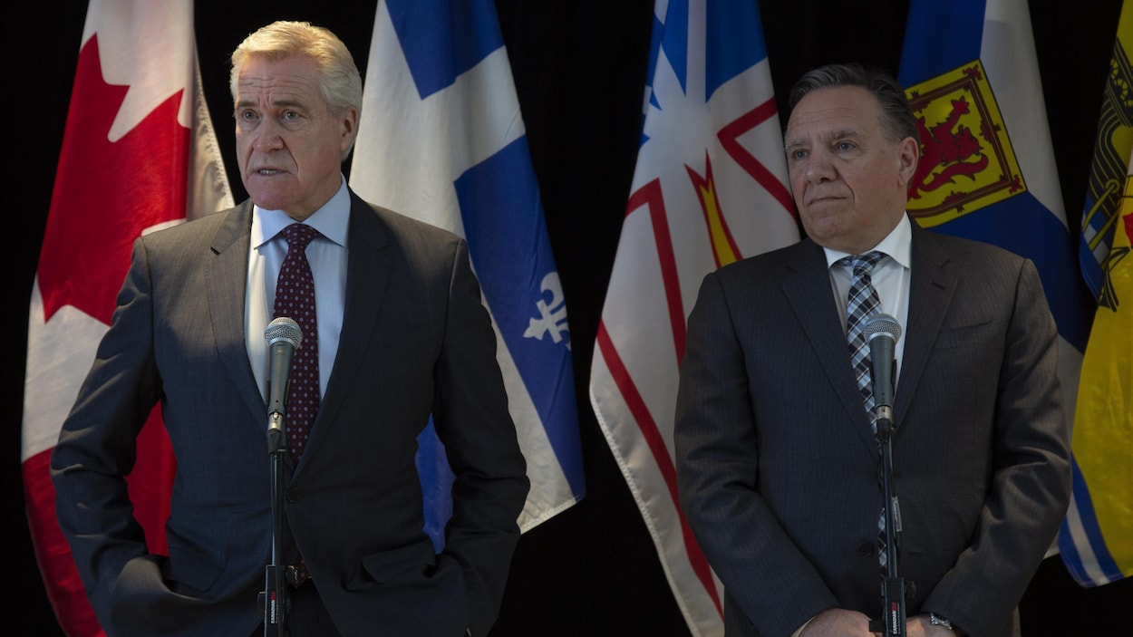 Les deux hommes, côte à côte, devant des drapeaux.