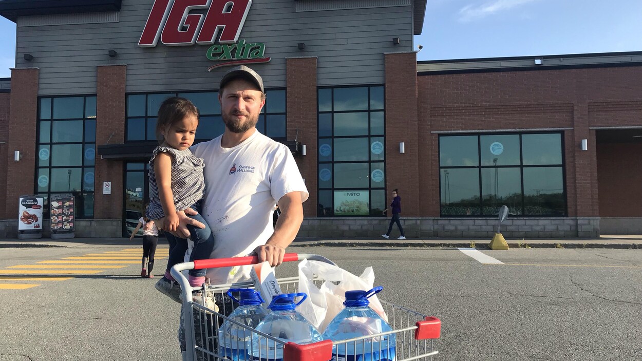 Un père et sa fille pousse un chariot rempli de bouteilles d'eau.