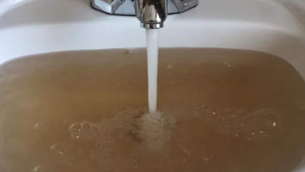 Un robinet qui laisse couler une eau brunâtre dans un lavabo.
