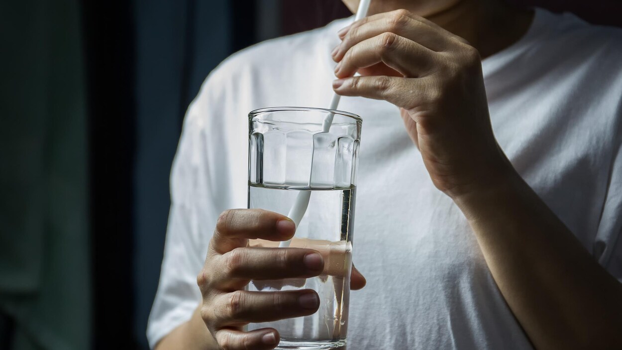 Une personne buvant de l'eau dans un verre à l'aide d'une paille. Une personne buvant de l'eau dans un verre à l'aide d'une paille.