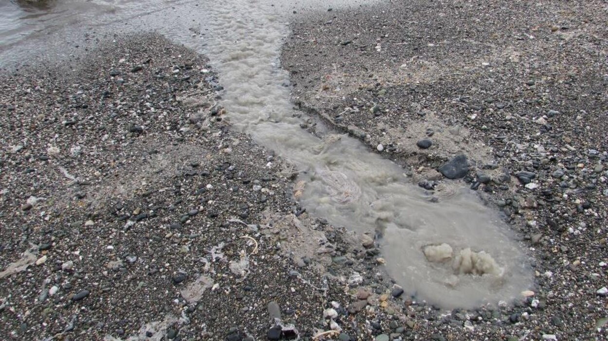 De l'eau grise jaillit d'un trou sur la plage, et s'écoule vers le fleuve. De l'eau grise jaillit d'un trou sur la plage, et s'écoule vers le fleuve.