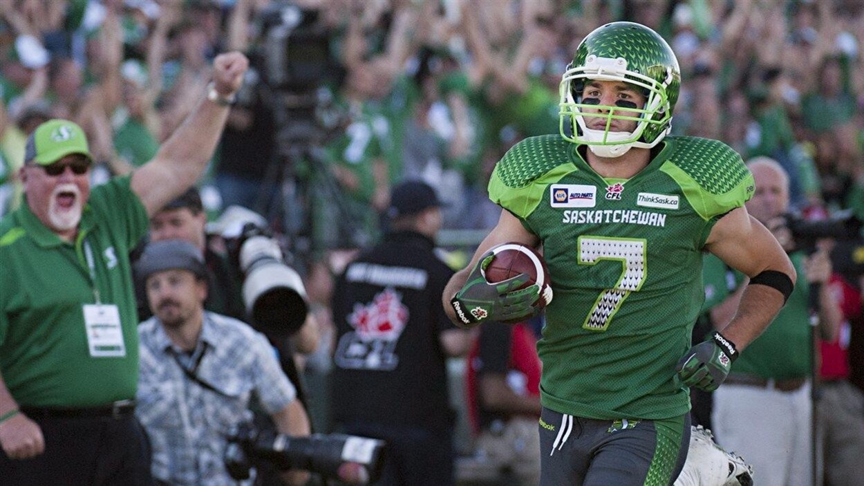 Un homme en habit de football vert avec un ballon dans les mains.