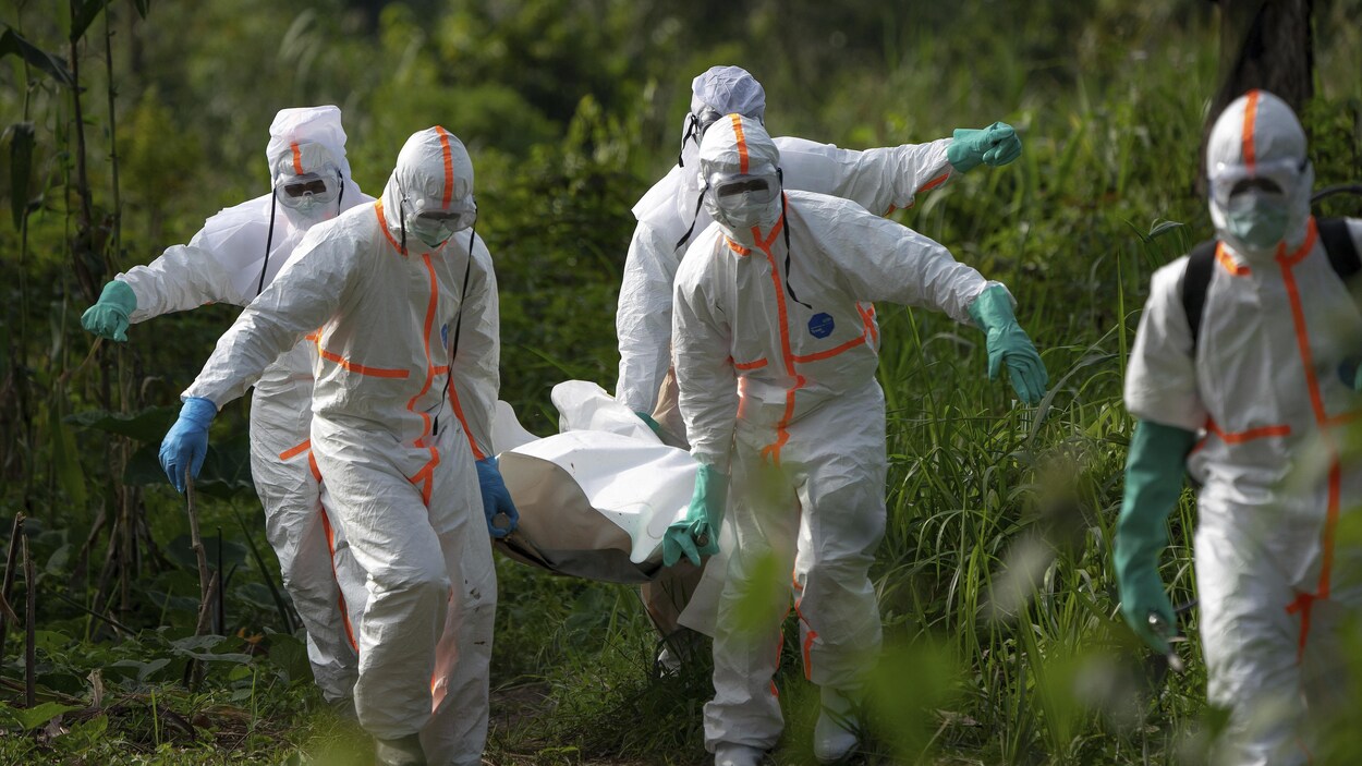 Des travailleurs funéraires en vêtements de protection portent les restes d’un homme mort d'Ebola.