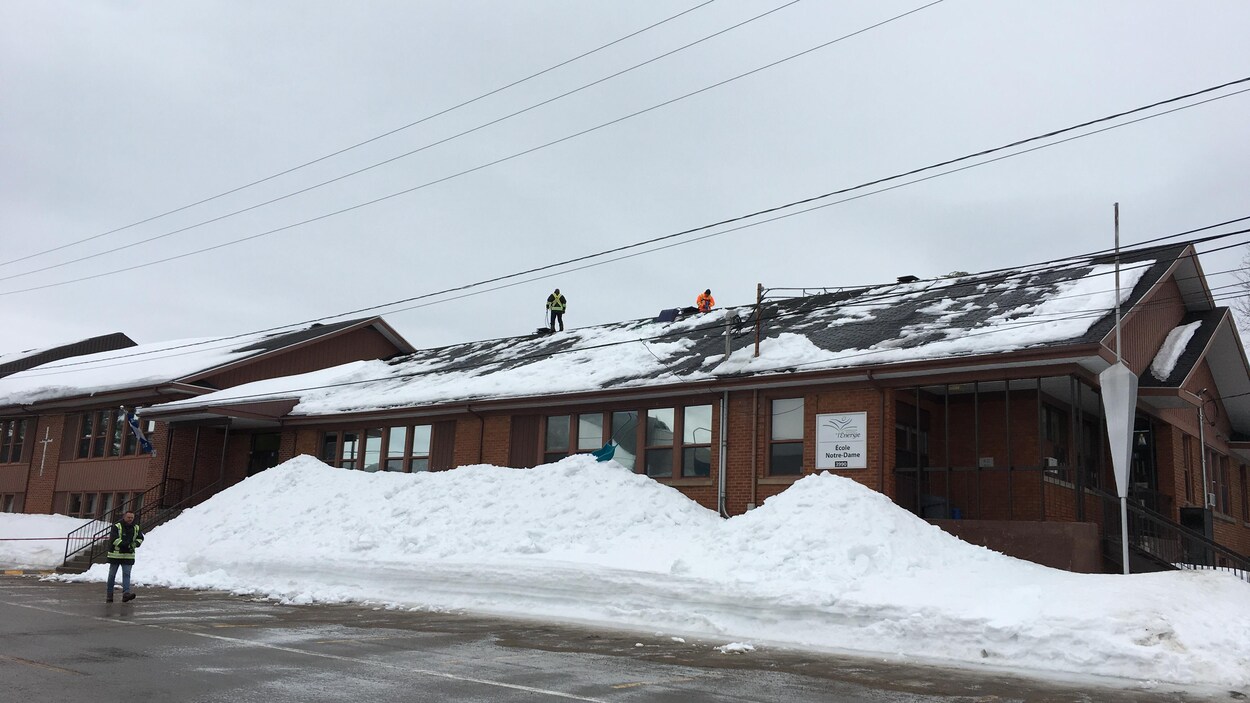 Des déneigeurs sont à l'oeuvre sur le toit de l'école.