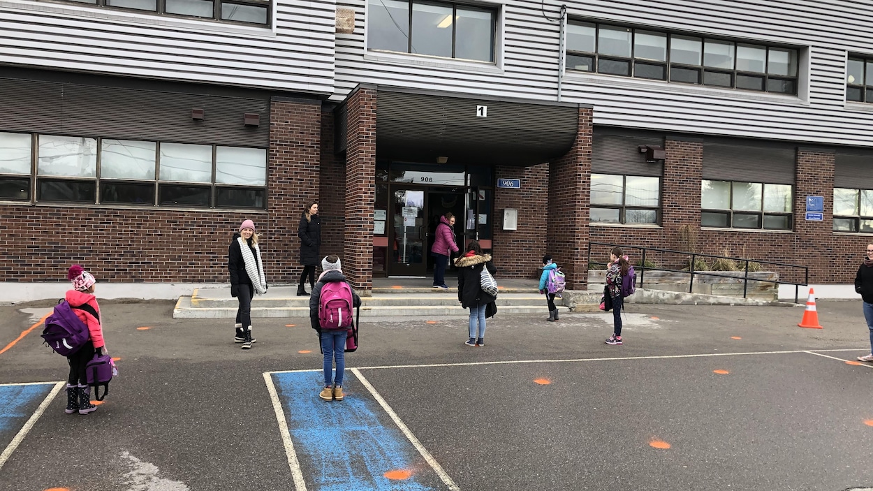 Des enfants loin les uns des autres attendent pour entrer dans l'école.