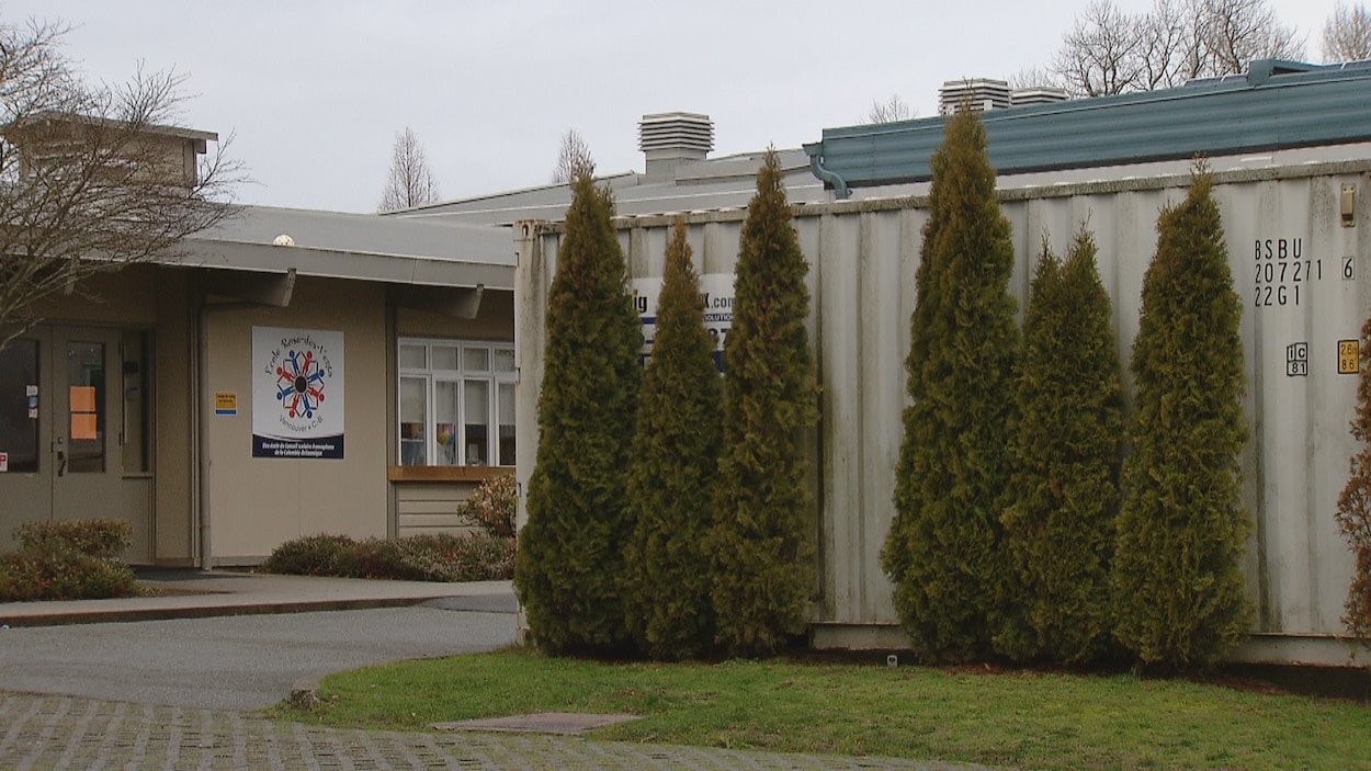 L'entrée de l'école vue de l'extérieur, avec le logo de l'école, et une partie d'un bâtiment un peu désuet avec quelques arbres devant.