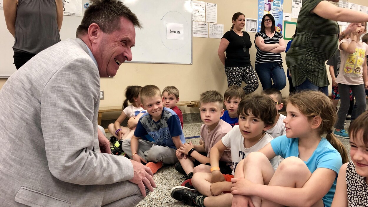 Un homme accroupi sourit à des enfants qui sont assis sur le sol d'une classe.