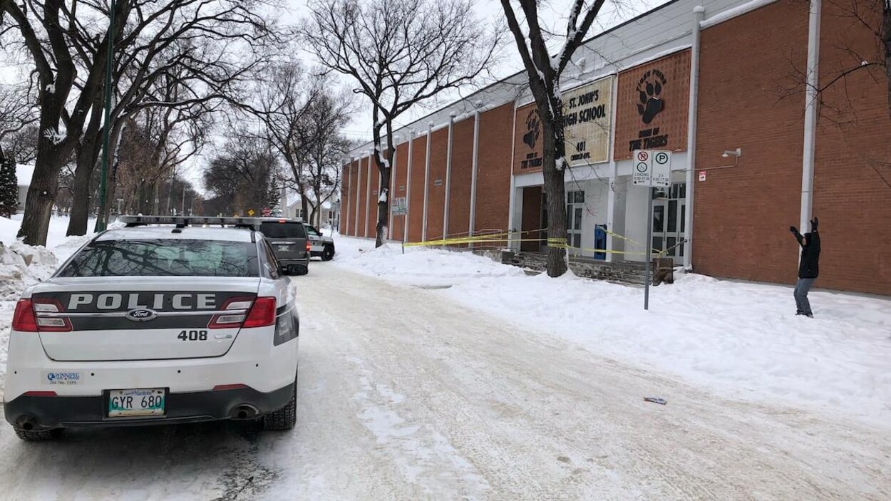 Des voitures de police sont stationnées sur la rue, devant une école.