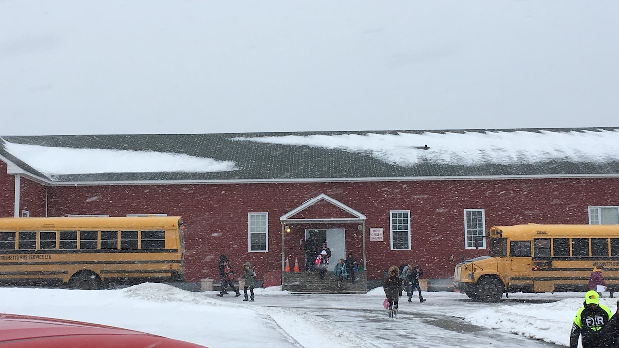 Des élèves sortent d'une école sous la neige. Des autobus attendent. Des élèves sortent d'une école sous la neige. Des autobus attendent.