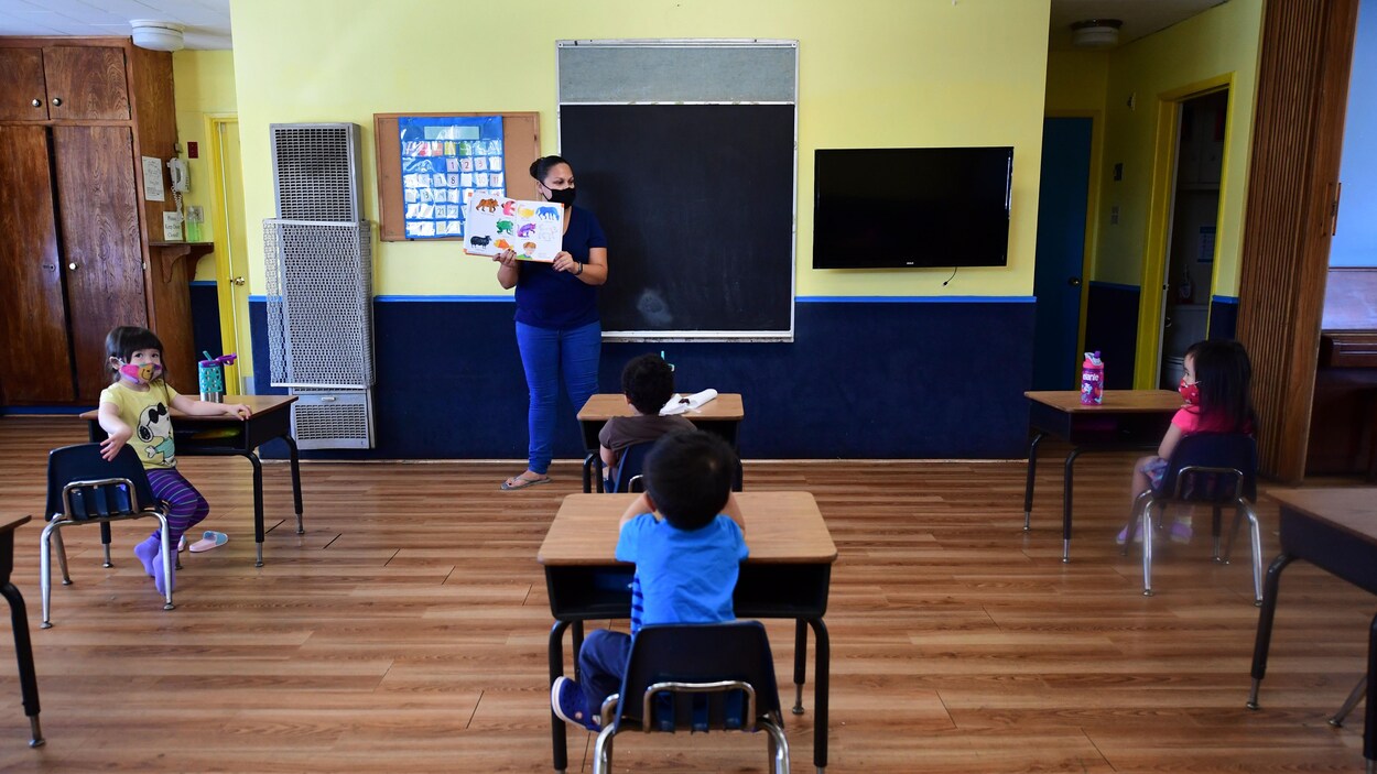 De jeunes élèves assis dans une salle de classe. Les pupitres sont positionnés à deux mètres de distance les uns des autres.