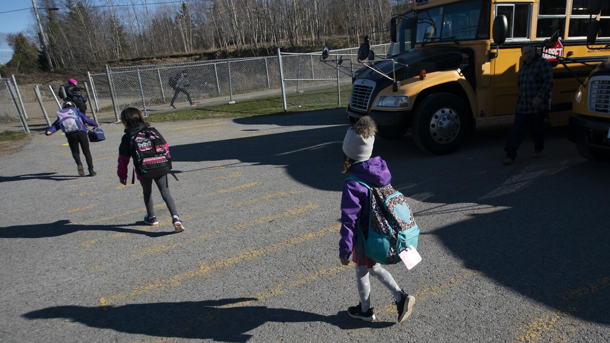 Des enfants gardent une bonne distance entre eux en longeant un autobus scolaire.