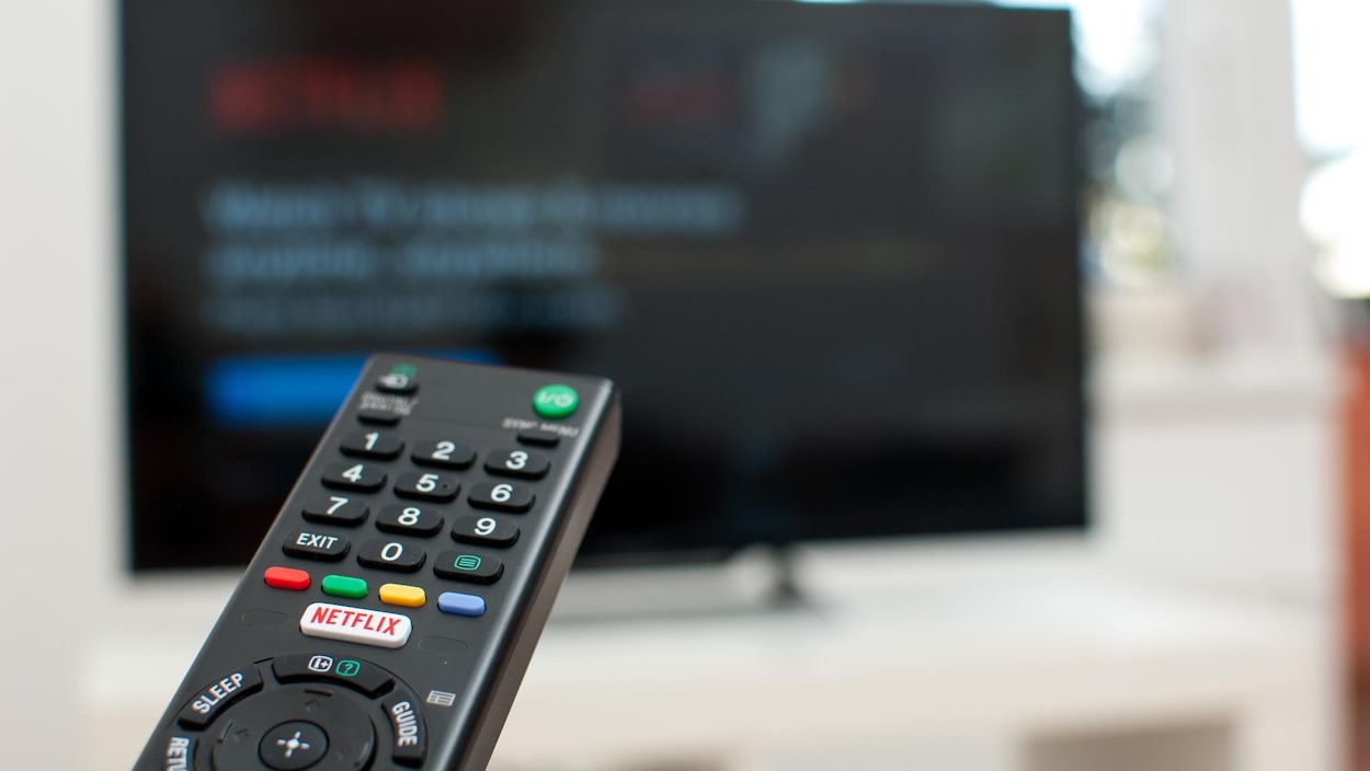 Une télécommande avec un bouton Netflix pointe vers un écran de télévision.