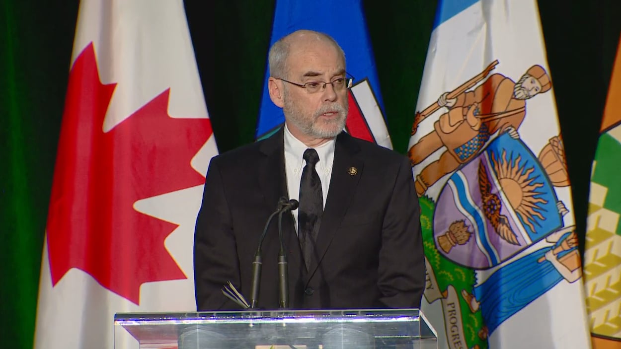 Fraser Forbes debout devant des drapeaux du Canada et de l'Alberta.