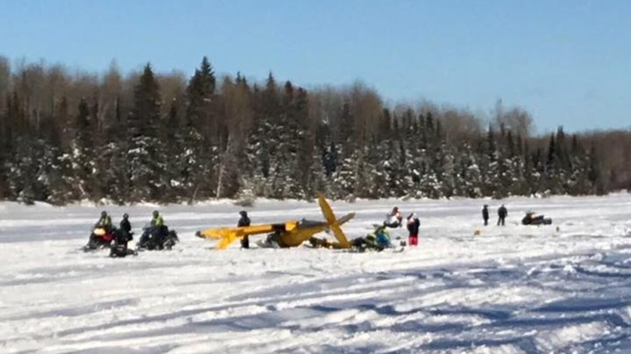Des motoneigistes sont regroupés autour d'un petit avion qui s'est écrasé sur un lac gelé.
