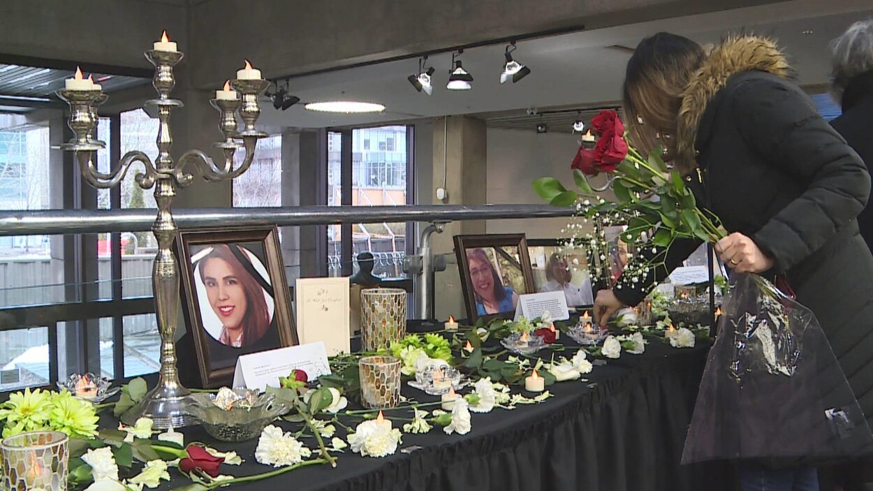 Des personnes déposent des fleurs sur une table où sont alignées des photos des victimes.