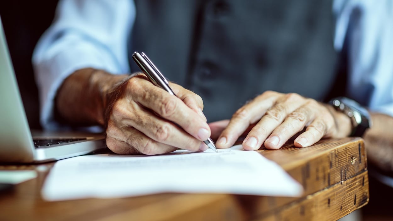 Plan serré des mains d'un homme âgé signant un document.