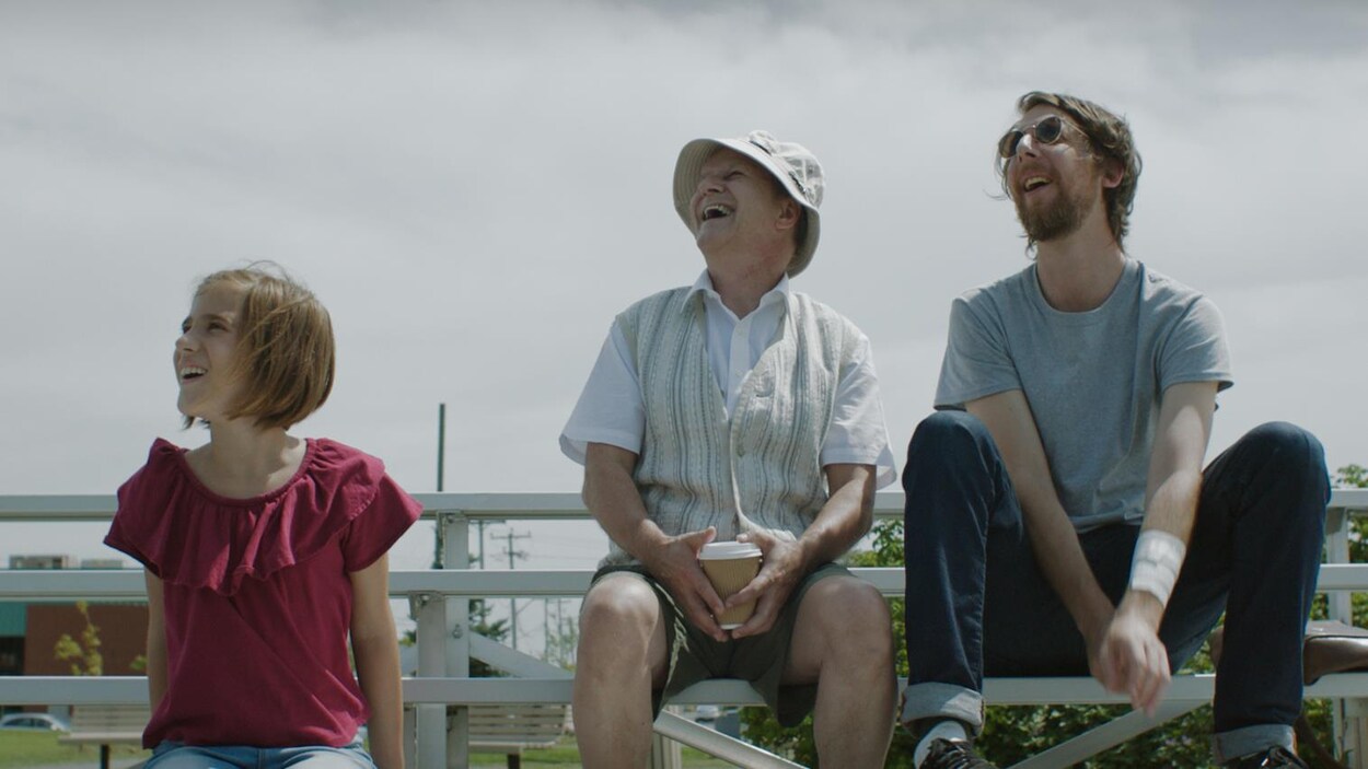 Trois personnage de la série Écrivain public sont assis dans des estrades en regardant le ciel, ébaubis. Trois personnage de la série Écrivain public sont assis dans des estrades en regardant le ciel, ébaubis.