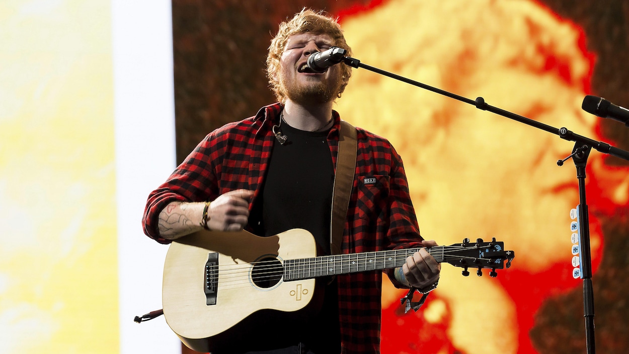 Ed Sheeran en train de chanter en tenant une guitare dans ses bras Ed Sheeran en train de chanter en tenant une guitare dans ses bras