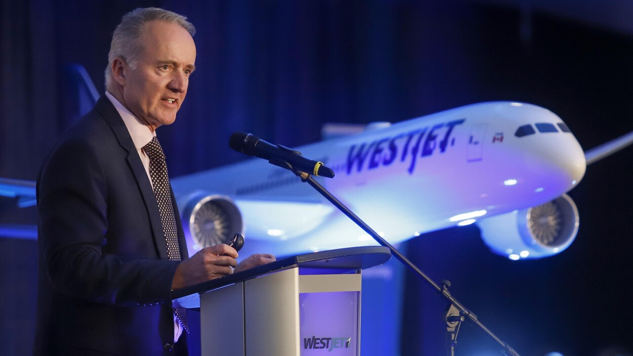 Le patron de WestJet, ED Sims, s'exprimant face à un micro avec un modèle d'avion en arrière-plan.
