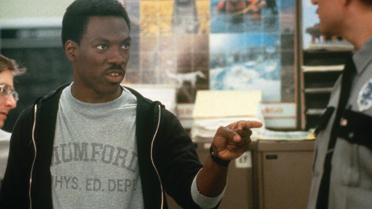 Dans une scène de film, un Eddie Murphy plus jeune montre un policier du doigt en lui parlant.